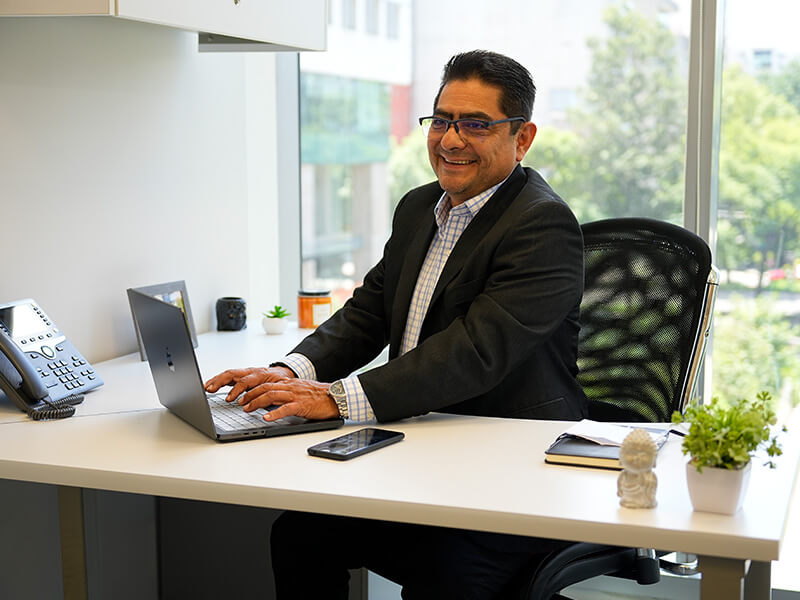 Hombre trabajando en escritorio con laptop junto a ventanal – Iza Office Club