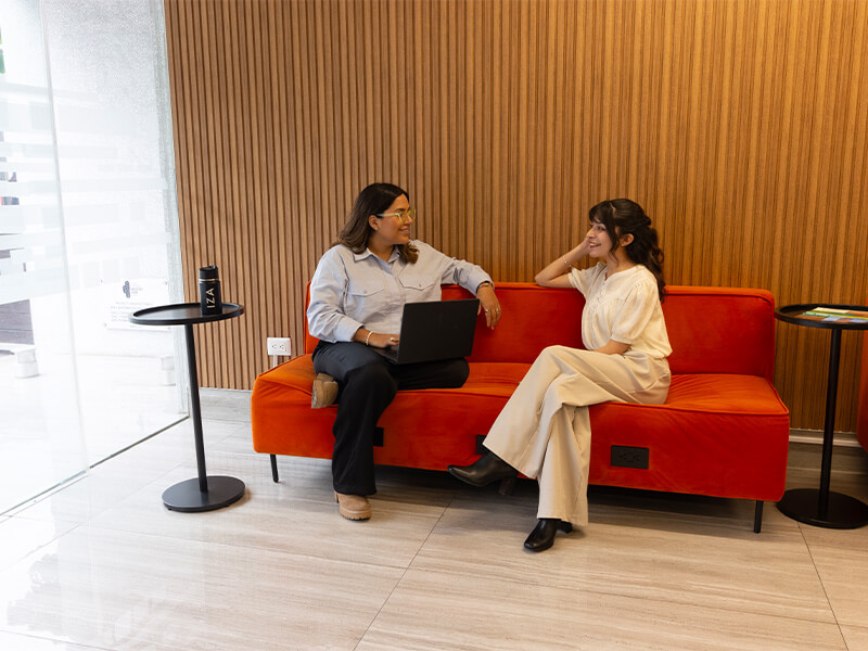 Dos mujeres conversando sentadas en sillones naranjas – Iza Office Club