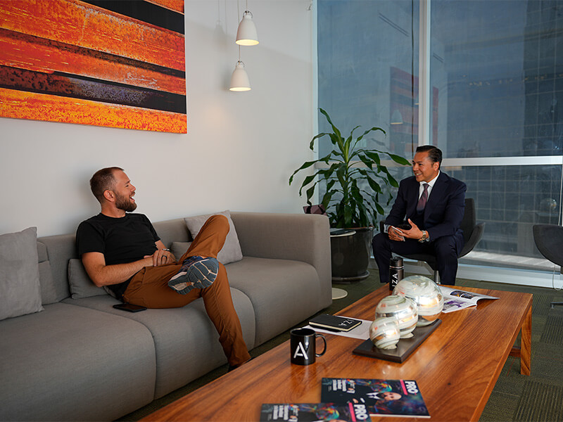 Dos hombres conversando sentados en sillón junto a mesa de centro – Iza Office Club