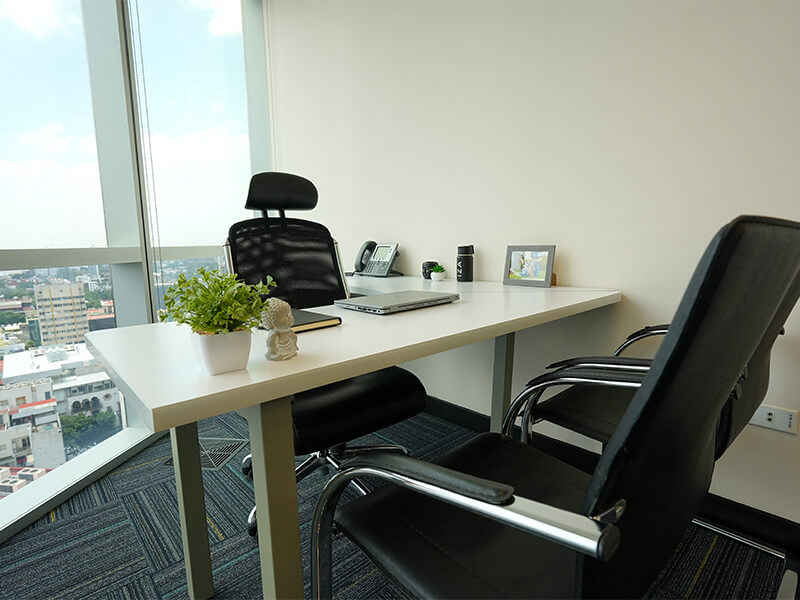 Escritorio en L con silla negra junto a ventanal con vista a la ciudad – Iza Office Club