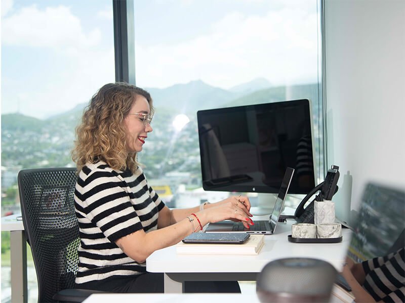 Mujer trabajando en escritorio con monitor doble – Iza Office Club
