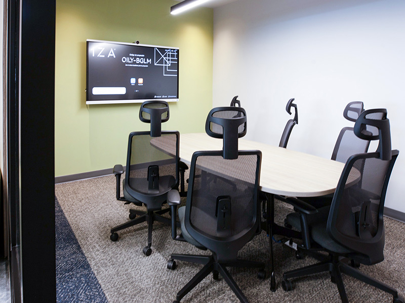 Pequeña sala de reuniones con mesa ovalada, sillas ergonómicas y pantalla mostrando el logo IZA en Inxignia, oficina en renta en Puebla