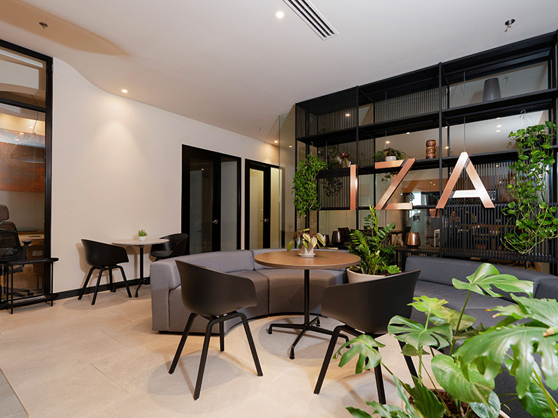 Área de descanso moderna en IZA Business Center con logo de la marca, cabinas privadas y plantas en Punto Sao Paulo, oficina en renta en Guadalajara