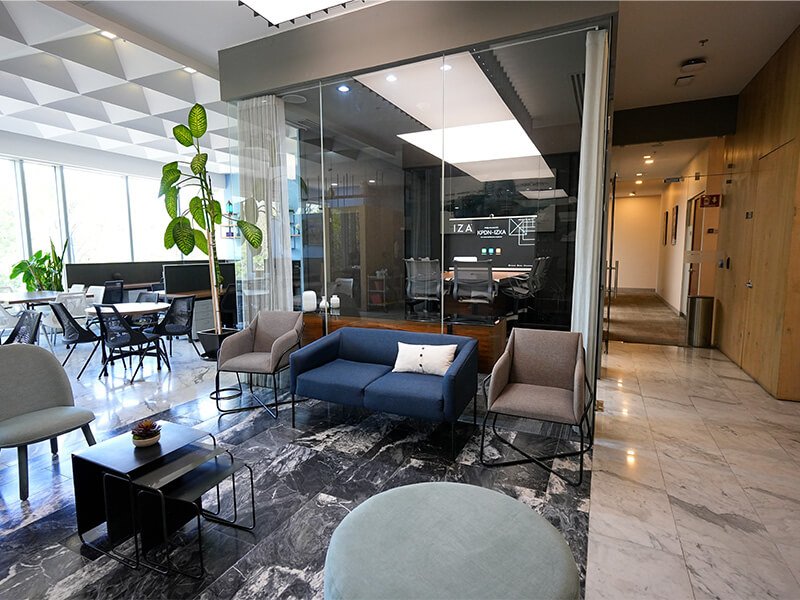 Área de lounge con sillones y sala de juntas de vidrio al fondo – Iza Office Club