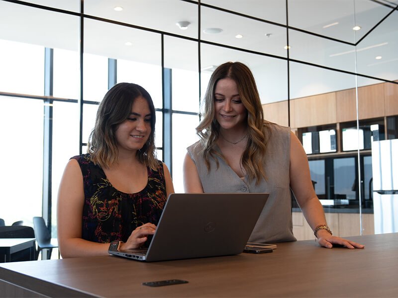 Dos mujeres sonriendo con laptop en escritorio – Iza Office Club