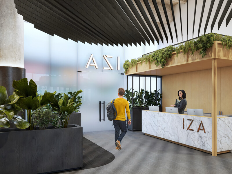 Hombre con suéter amarillo caminando hacia el mostrador de recepción de IZA en URBAN CENTER CANCUN, donde lo espera una recepcionista.