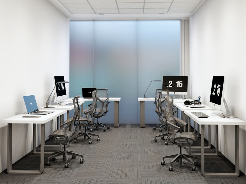 Fotografía del interior de IZA Urban Center Cancún, mostrando una moderna oficina privada equipada con escritorios blancos, computadoras iMac, laptops y sillas ergonómicas, con un gran ventanal de cristal esmerilado al fondo.