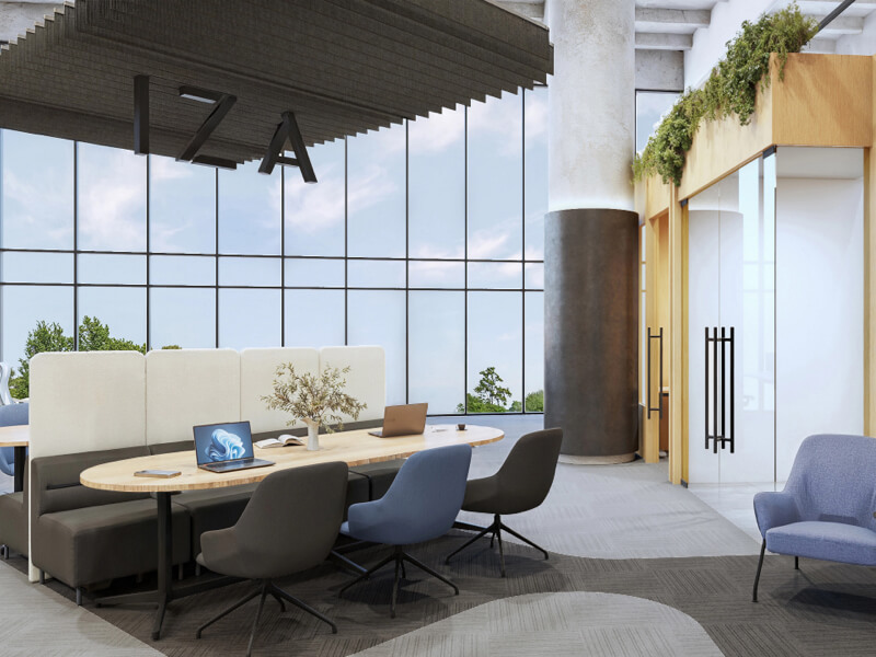 Fotografía del interior de IZA Urban Center Cancún, mostrando un área de coworking moderna con una mesa de trabajo ovalada, laptops, sillas ergonómicas y un sillón, complementado con grandes ventanales y las letras de 